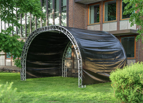Black arched outdoor stage canopy set on green lawn.