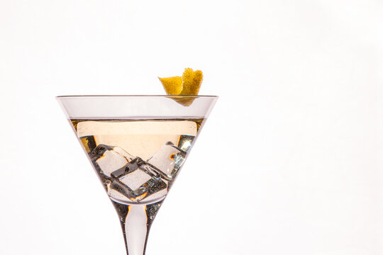 golden martini with icecubes and lemon cest as a garnisch on white background.