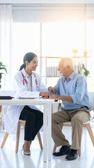Fototapeta premium A caring female doctor smiles warmly while holding the hand of an elderly senior patient in a bright medical clinic, evoking trust, empathy, and professional healthcare support.
