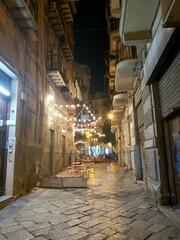 Fototapeta premium PALERMO, SICILY, ITALY Narrow street in Palermo old town at night with restaurants, lights, historic buildings and wet cobblestone pavement