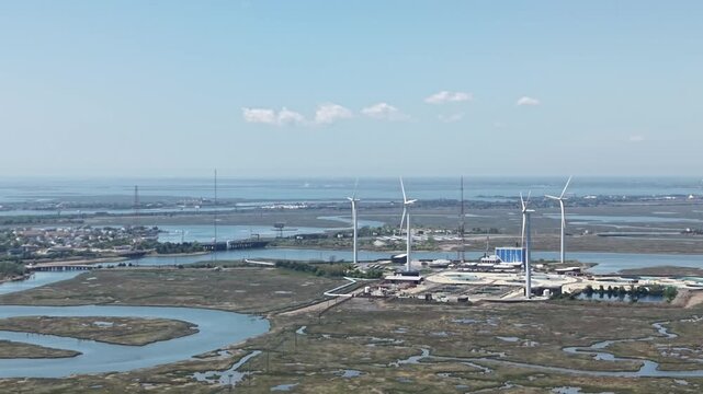 Drone view of wind farm with 5 spinning turbines pan left view of surrounding bay marsh