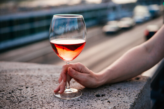 Hand holding a glass of rose wine in summer sunshine during a outdoors party or a picnic.