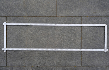 Fototapeta premium White Folding Ruler Formed into a Rectangle Shape, Lying on Patio Paving Slabs, Construction Measurement and Geometric Layout Concept