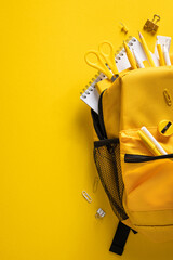 Obraz premium Yellow backpack filled with school supplies for back to school and organized study essentials on vertical vibrant background