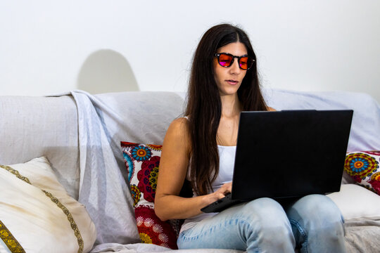 Woman wearing red lens blue light glasses working on laptop for eye protection