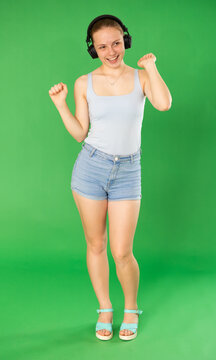 Young woman in casual clothes listens to music in modern headphones with high-quality sound on a chroma key background. Girl who is engaged in dancing enjoys her favorite song on a green background