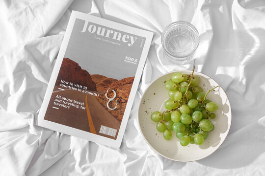 Plate with sweet ripe grapes, magazine and glass of water on white fabric background