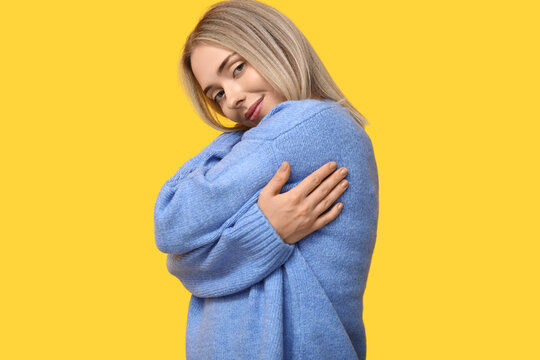 Young woman hugging herself on yellow background