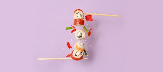 Fototapeta premium Floating sushi rolls with chopsticks on purple background