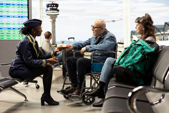 Flight attendant assists an elderly man in a wheelchair and his wife at an airport gate, ensuring accessibility and guidance during retirement travel.