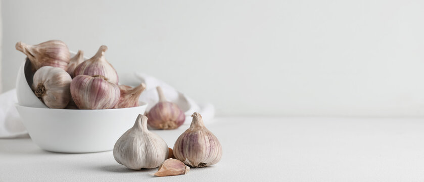 Fresh garlic bulbs in white bowls on white surface