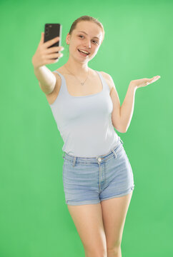 Teenage girl in blue top takes selfie on a smartphone on a green background. Chroma key compositing