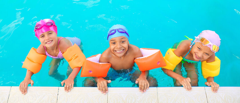 Three children swimming in pool with floaties and swim caps