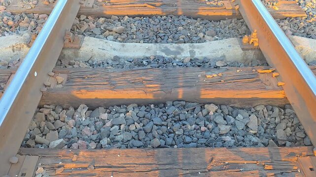 Low angle video of endless railway tracks with wooden and concrete sleepers stretching into the distance at sunset through a spring forest. Concept of travel and journey