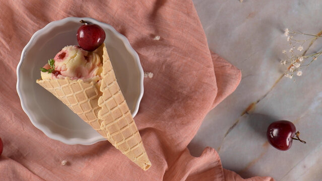 Ice cream scoop with cherry in a waffle cone on a ceramic plate