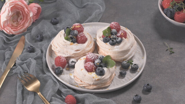 Three mini pavlova meringues topped with fresh raspberries and blueberries on a grey plate
