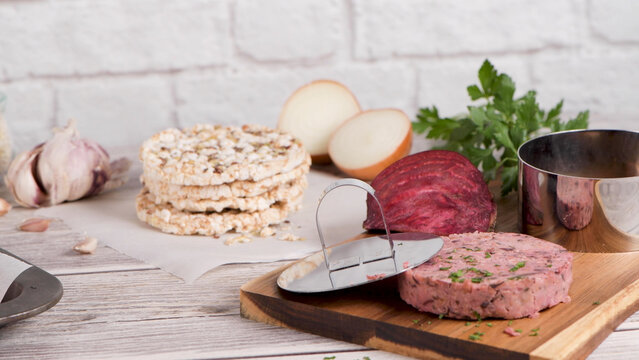 Raw vegan vegetable burger patty with fresh ingredients on a wooden board