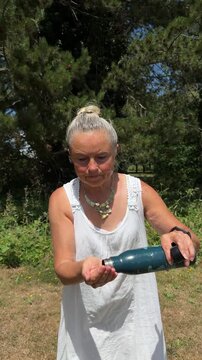 Active senior woman pouring fresh water from a bottle on her face and hair to cool down during summer heatwave.