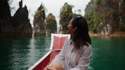 Fototapeta premium Joyful woman exploring towering limestone karsts by boat at khao sok lake, thailand