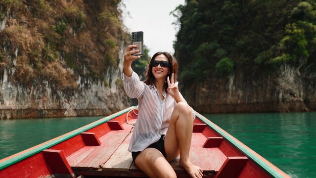 Young woman taking selfie on longtail boat enjoying tropical khao sok lake vacation