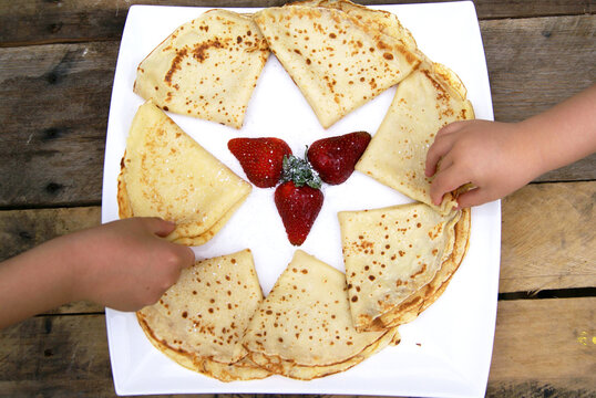 Overhead view of two children sitting at a wooden garden table sharing a plate of homemade folded pancakes with fresh strawberries