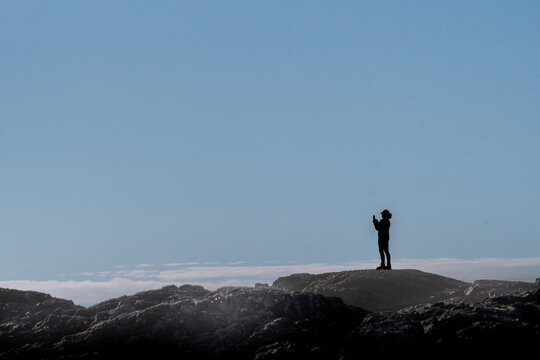 Side view silhouette of a Woman standing on a Bluff taking a photo with a mobile phone, British Columbia, Canada