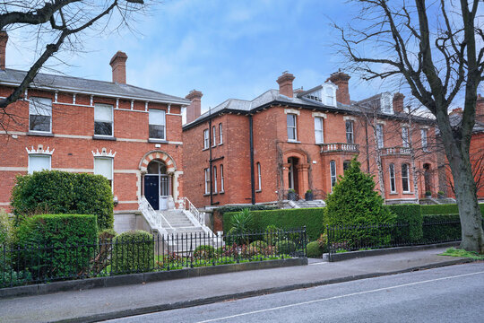 row of large brick townhouses with bay windows and fenced front yards
