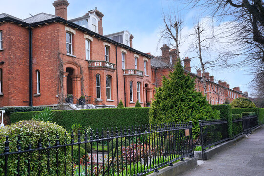 Long row of large brick townhouses with bay windows and fenced front yards