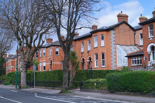 row of arge brick townhouses with bay windows and tall hedge around front yards