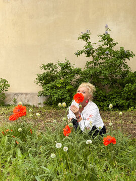 Smiling woman crouching in a garden and hiding her face behind a red poppy