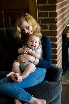 Portrait of a woman in jeans sitting on a sofa with her smiling baby son on her lap