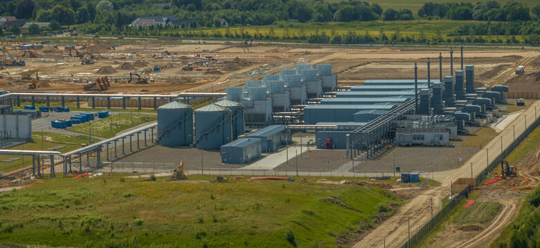 Aerial view of data center cooling infrastructure with cooling towers, water storage tanks, industrial piping systems, and utility buildings within a high-tech industrial complex under construction.