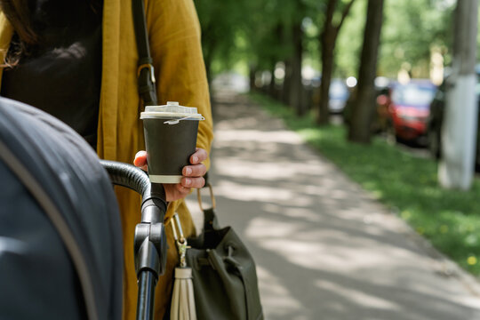 Close-up of a woman holding a cup of coffee while pushing a stroller in a park on a sunny day