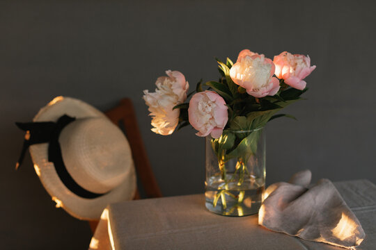 Close-up of a bunch of pink peonies in a vase and napkin on a table with a straw hat hanging on a chair