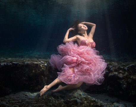 Young woman in an off shoulder pink evening gown sitting underwater on a riverbed, Florida, USA