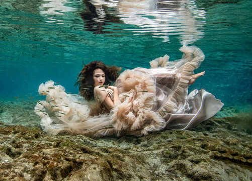 Young woman in an elegant evening gown floating underwater over a riverbed, Florida, USA