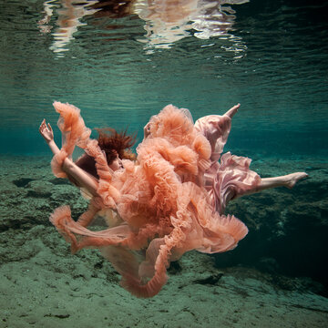 Young woman in an elegant orange evening gown floating underwater over a riverbed, Florida, USA