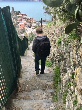 Rear view of a young man walking down cobblestone stairs toward the Ligurian Sea, Vernazza, Cinque Terre, Liguria, Italy
