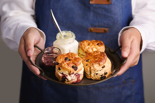 Close-up of a woman carrying a tray of Freshly Baked Scones with clotted cream and blueberry jam for Afternoon Tea