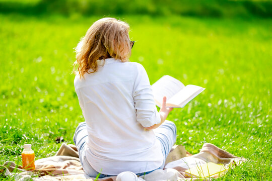 Woman with textbook from behind on grass for backyard summer study. Solitude relaxation and mindful literature reader concept in park.