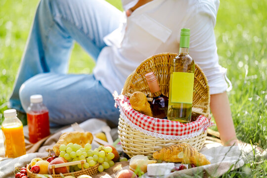 Woman at wine picnic sits near basket on green grass. Summer outdoor degustation and countryside leisure concept.