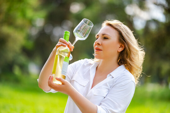Woman expert tasting Riesling wine and examining bottle on outdoor degustation. Professional sommelier evaluation and beverage quality concept.