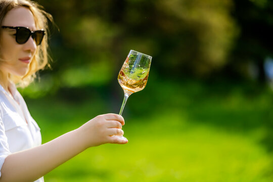 Woman expert in sunglasses examining a swirling glass of amber wine outdoors. professional sommelier tasting and quality evaluation concept.