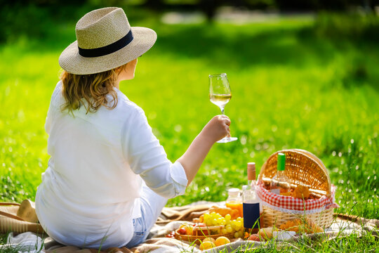 Woman in straw hat holding a wine glass at a luxury backyard picnic. Countryside summer vacation and premium outdoor dining concept.