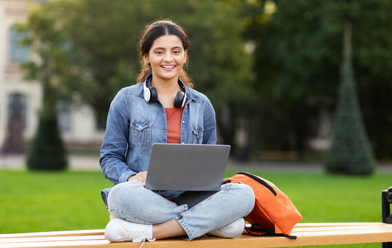 Serene indian woman zoomer studies on a campus bench with laptop, showcasing the blend of eastern culture and modern education techniques