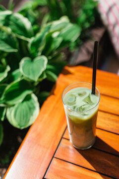 Close-up of an iced matcha latte with a drinking straw on a garden table on a summer day