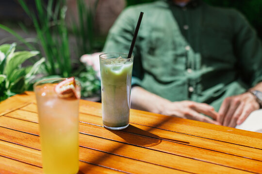 Close-up of a man sitting at a cafe table on a summer day with an iced matcha latte