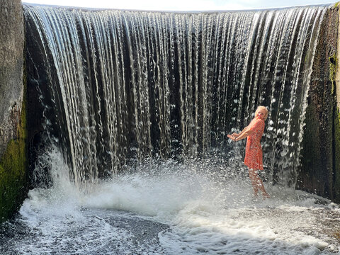 Side view of a woman standing in the Kumeciu waterfall on a summer day, Alytus, Lithuania