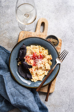 Overhead view of a Bowl of ravioletti pasta with tomato sauce, cheese and a glass of white wine on a wooden chopping board
