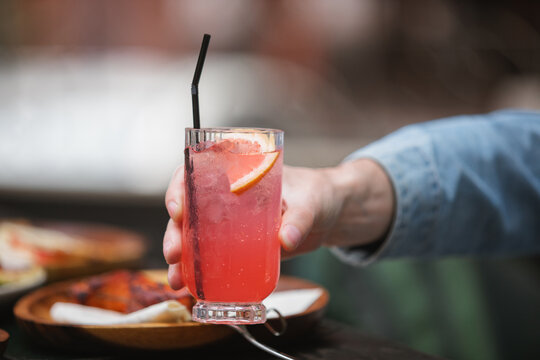 Close-up side view of a man sitting at an outdoors caf&eacute; holding a grapefruit lemonade drink